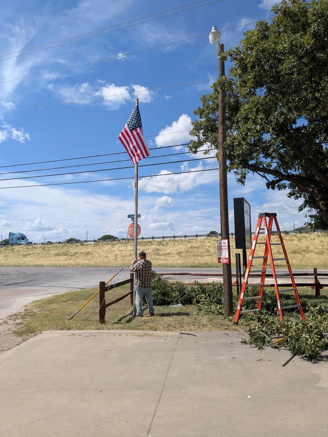 A man raising a new American flag at the park entrance on a sunny day beside the I-20 access road
